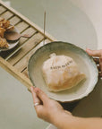 Person holding a bowl with a bath ritual package on a wooden tray.
