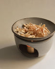 Handcrafted ceramic oil burner with Palo Santo bath flakes in the top dish, candle lit underneath