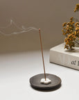 Burning a Palo santo incense in a ceramic holder, with dried flowers and an open book placed in the back, creating a peaceful, contemplative atmosphere.