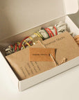 Open box of sacred burning ritual kit showing white sage, Palo Santo wood sticks, incense sticks, and labeled kraft envelope with brass incense holder