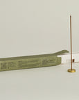 burning cedar incense stick with a brass holder and opening package behind