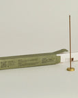 burning cedar incense stick with a brass holder and opening package behind