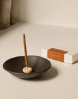 Burning cinnamon incense stick in a black ceramic bowl with box