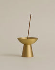 polished brass conical incense holder with an incense stick burning, creating a sleek and serene atmosphere