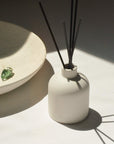 Ceramic jar diffuser with reed sticks, accompanied by a crystal quartz placed on a ceramic bowl nearby.