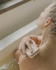 Person scrubbing their shoulder with a bar of soap in a bathtub.
