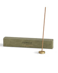 Sandalwood incense stick with a brass incense holder and the packaging behind
