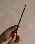 Hand gently holding smoldering Black Copal incense stick with soft smoke