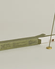 burning hinoki incense stick with brass holder and opening packaging box behind