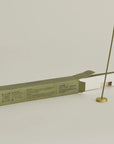 burning hinoki incense stick with brass holder and opening packaging box behind