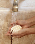 Hands holding a bar soap under running water from a faucet