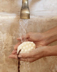 Hands holding a bar soap under running water from a faucet
