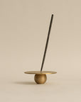 A brass orb incense holder with an incense stick inserted, perfect for a contemporary incense ritual