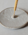 an incense stick and light grey ceramic incense holder