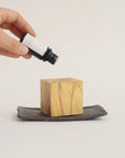 Dropping Palo Santo essential oil onto a cubic natural wood diffuser, enhancing the calming aroma for a peaceful atmosphere