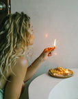 Woman performing a mindful ritual by lighting Palo Santo bath flakes after a bath, showing Cedar and Myrrh’s dual-use Palo Santo Flake and Essential Oil Set for bathing and burning rituals