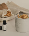 Ceramic oil burner with Palo Santo bath flakes, Palo Santo essential oil placed alongside, and additional bath flakes in a bowl behind, perfect for a calming experience
