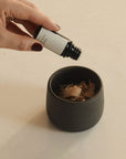 Dropping essential oils onto Palo Santo flakes in a raw black clay incense smudging cup to create a soothing aroma