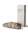 organic white sage bundle tied with multicolored string placed next to a box labeled organic white sage cleansing and purifying
