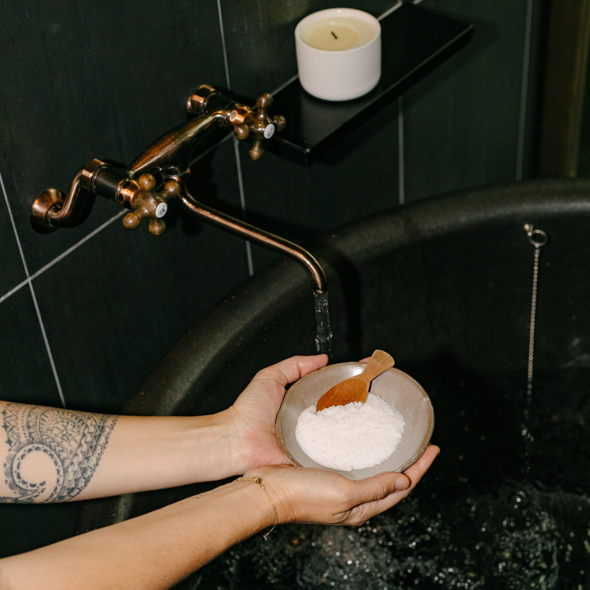 Cedar and Myrrh Sacred Bath Salts held in a ceramic bowl with a wooden scoop over a black soaking bathtub, creating a calming and intentional self-care bathing ritual.