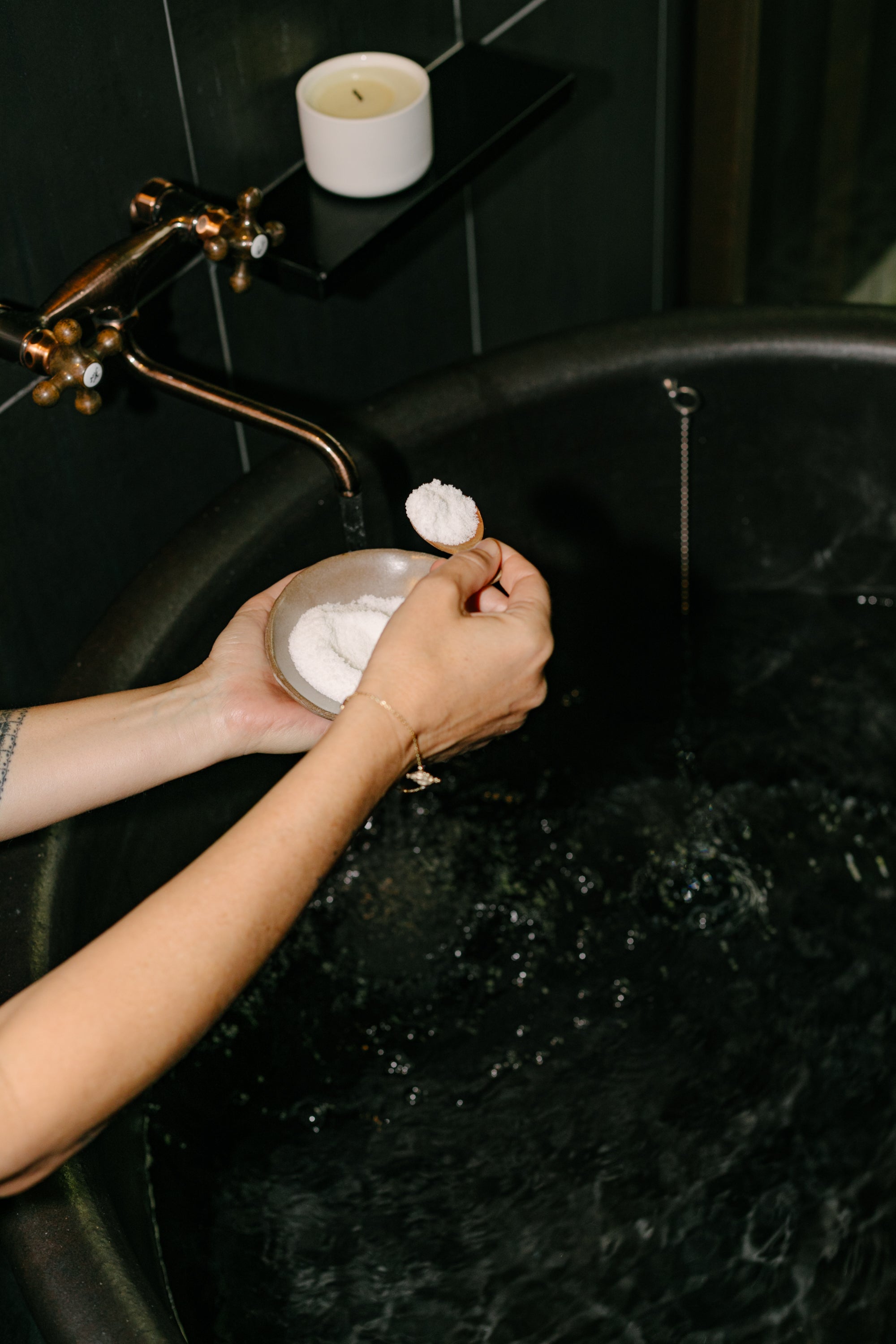 Person holding a bowl of soapy water in a dark bathroom with a candle on a shelf.