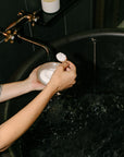 Person holding a bowl of soapy water in a dark bathroom with a candle on a shelf.