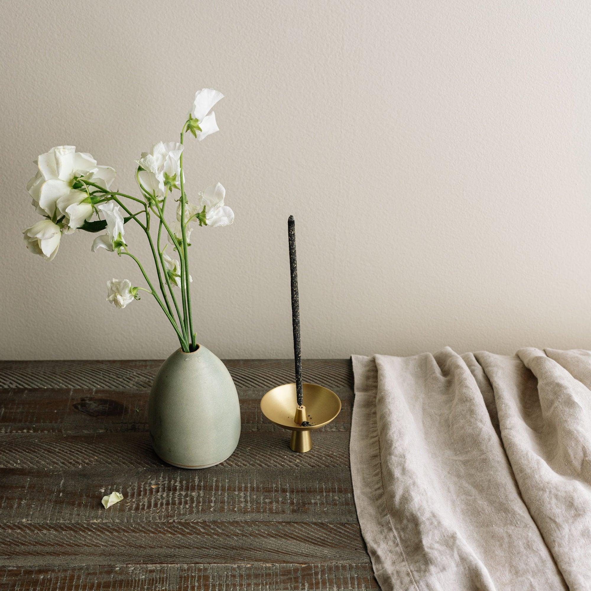 flower vase,  brass ash catcher with an incense holder, linen cloth on the wooden table