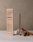 Left: package of cinnamon incense; Right: burning incense stick with incense holder and 3 pieces of cinnamon roll sticks and a rock.
