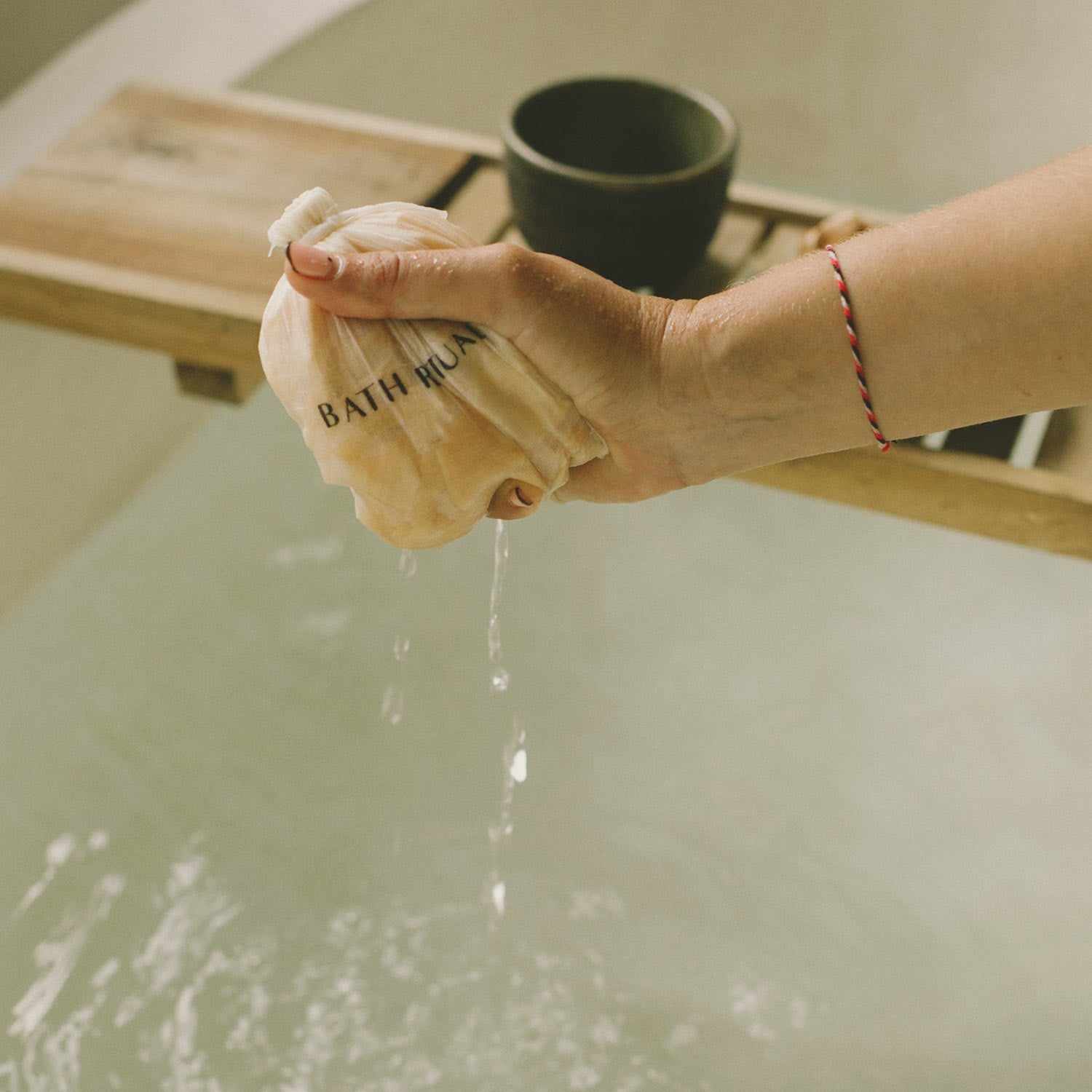 Person squeezing a bath mug filled with water over a bathtub.