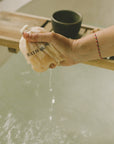 Person squeezing a bath mug filled with water over a bathtub.
