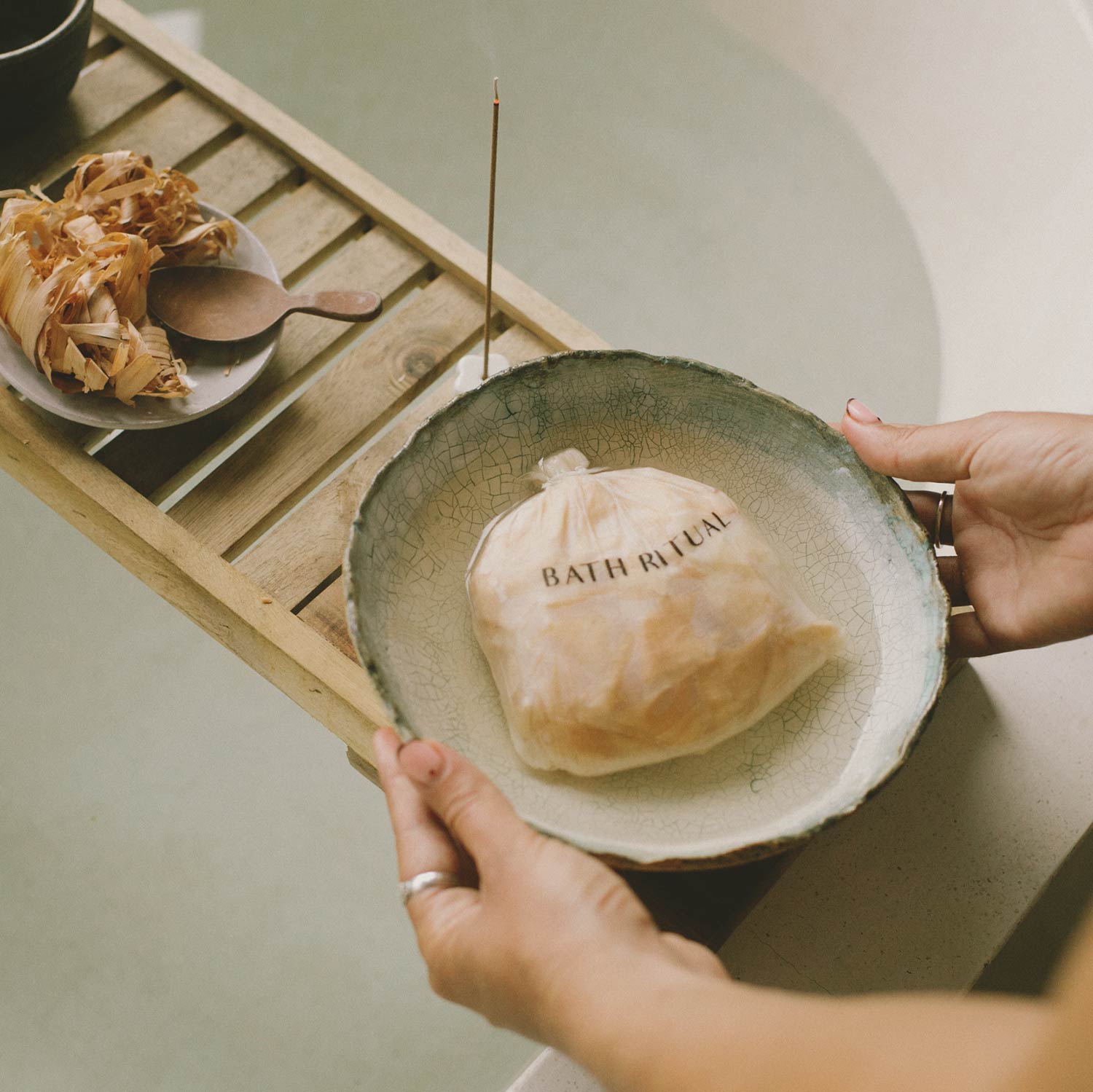 Person holding a bowl with a bath ritual package on a wooden tray.