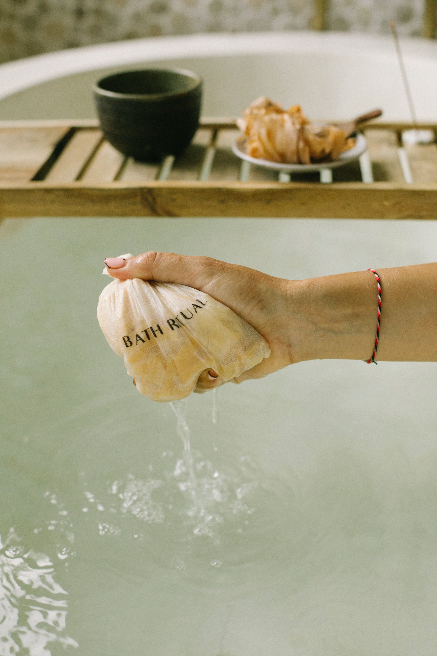 Woman squeezing Hinoki bath tea bag in warm water for stress relief, enjoying the calming aroma of Japanese Hinoki wood during a mindful bath ritual by Cedar and Myrrh