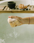 Woman squeezing Hinoki bath tea bag in warm water for stress relief, enjoying the calming aroma of Japanese Hinoki wood during a mindful bath ritual by Cedar and Myrrh