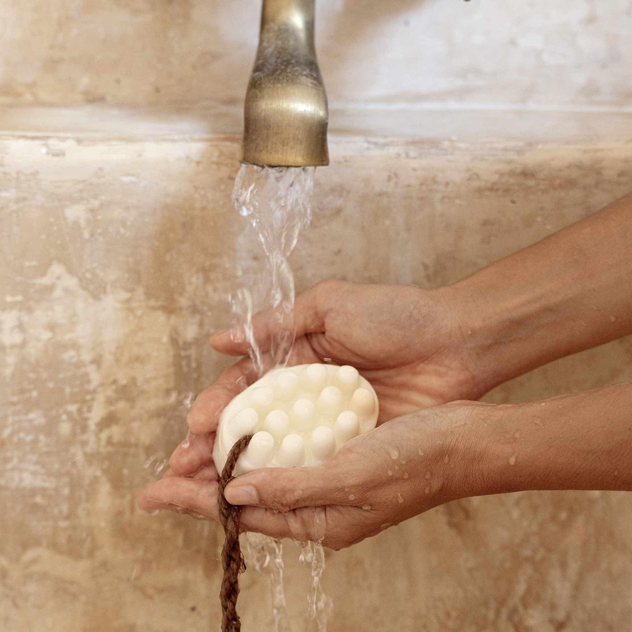 Hands holding a bar soap under running water from a faucet