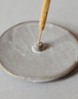 an incense stick and light grey ceramic incense holder
