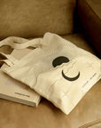 canvas tote bag with celestial print placed on the sofa with book