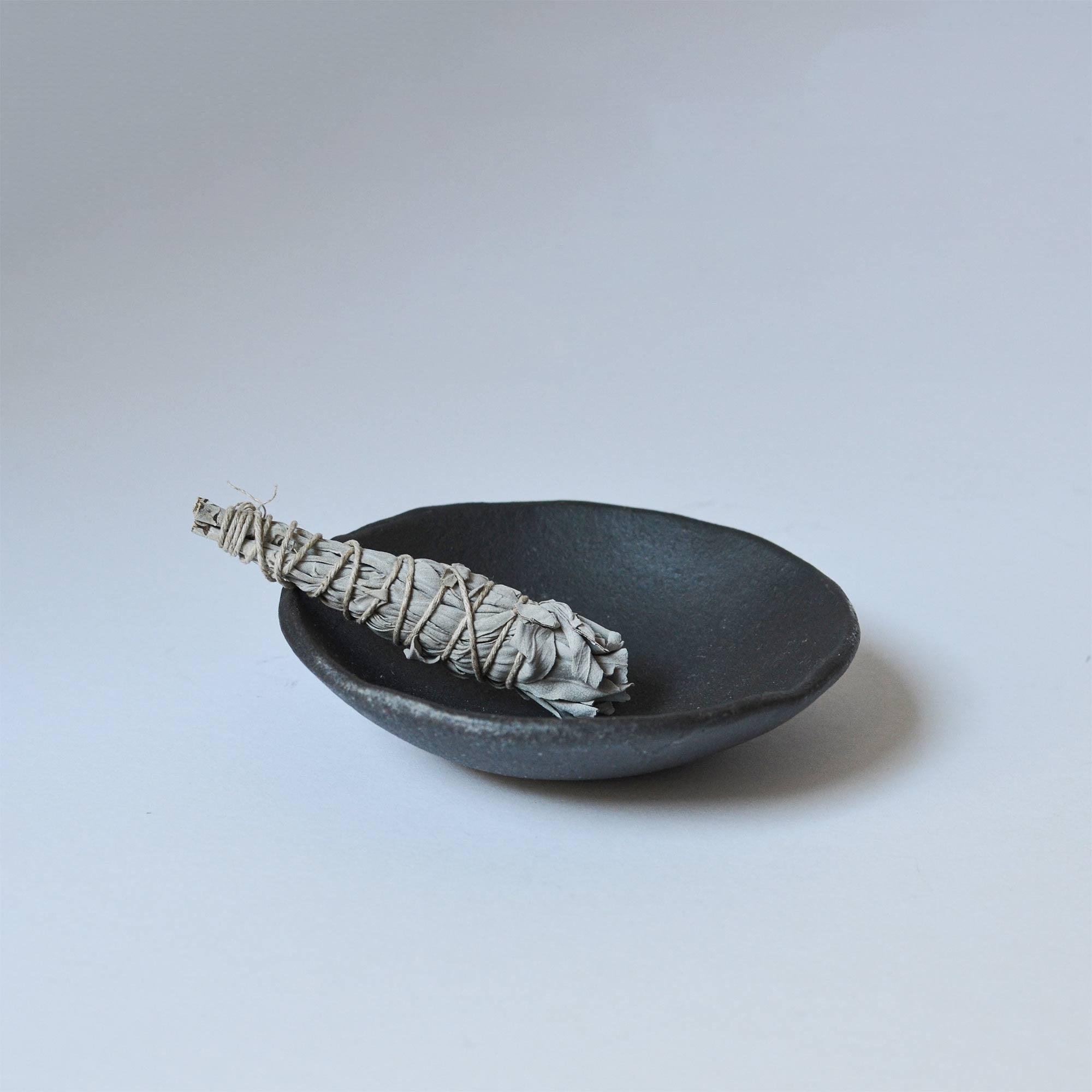 Mini white sage smudge stick on the raw black clay smudging bowl.