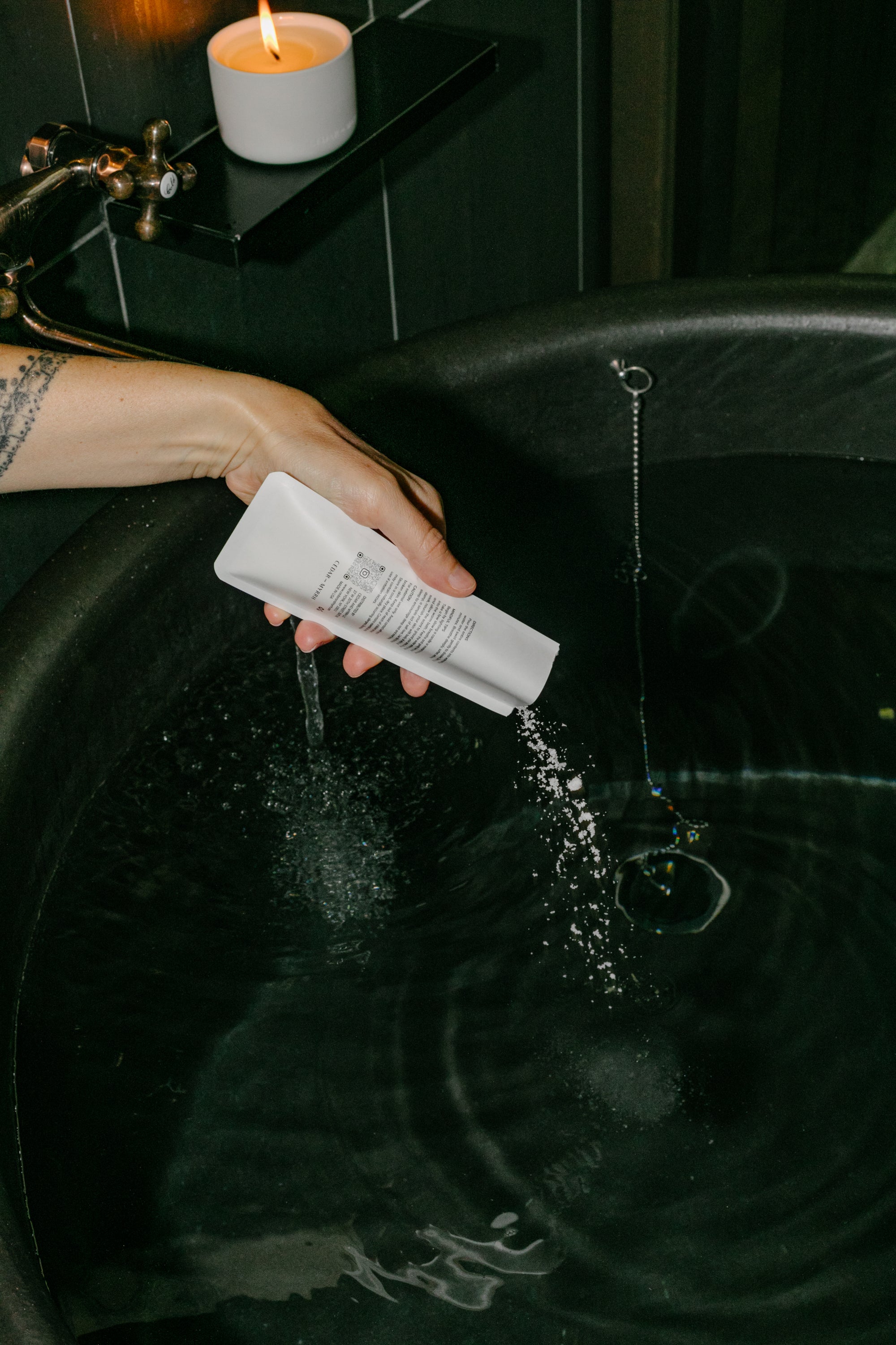 Person pouring Cedar and Myrrh Palo Santo bath salt into warm water during a candle-lit bath ritual for relaxation and mindfulness