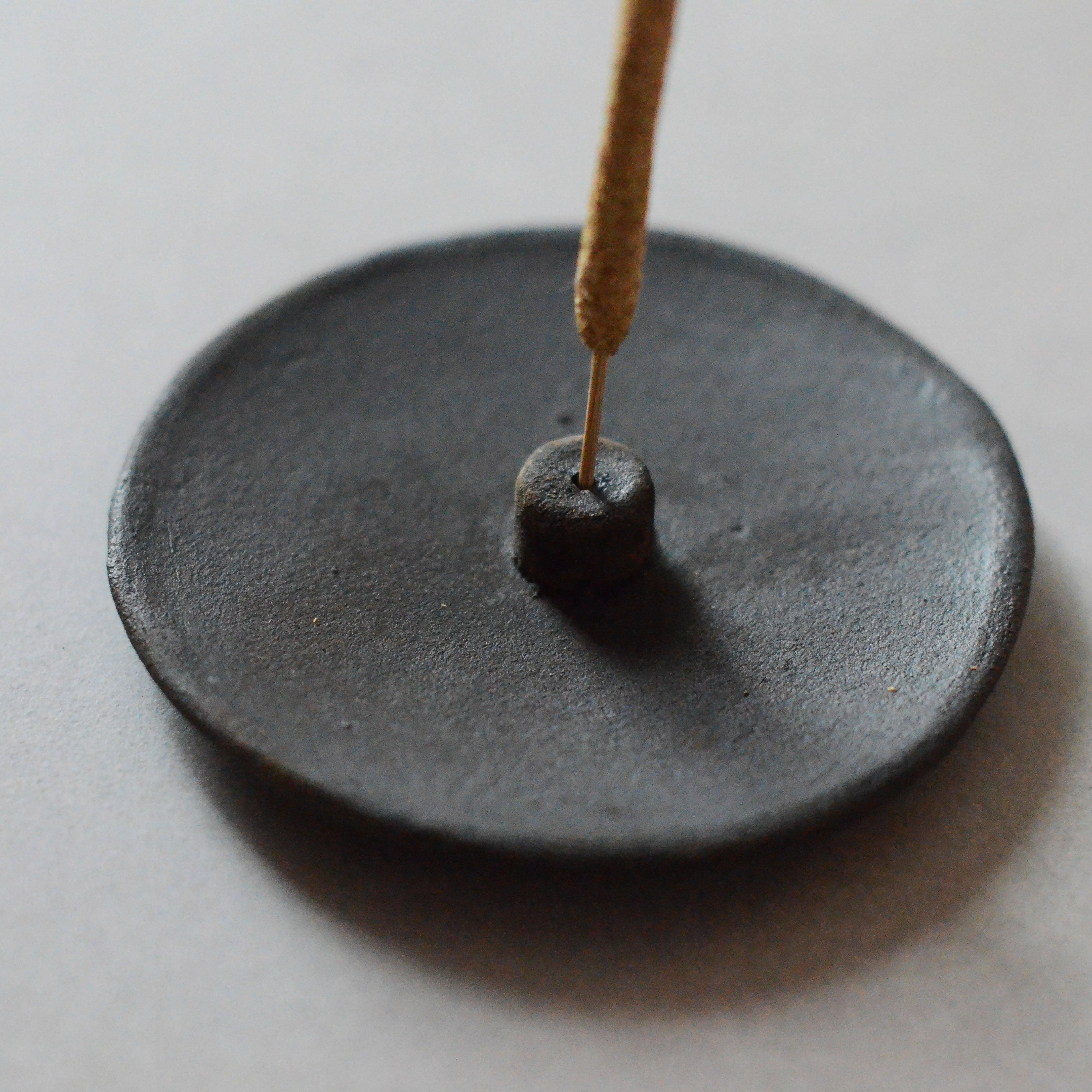 an incense stick and a raw black clay incense holder
