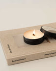 lighting a travel size wellness candle with a lid and placed on the top of the book