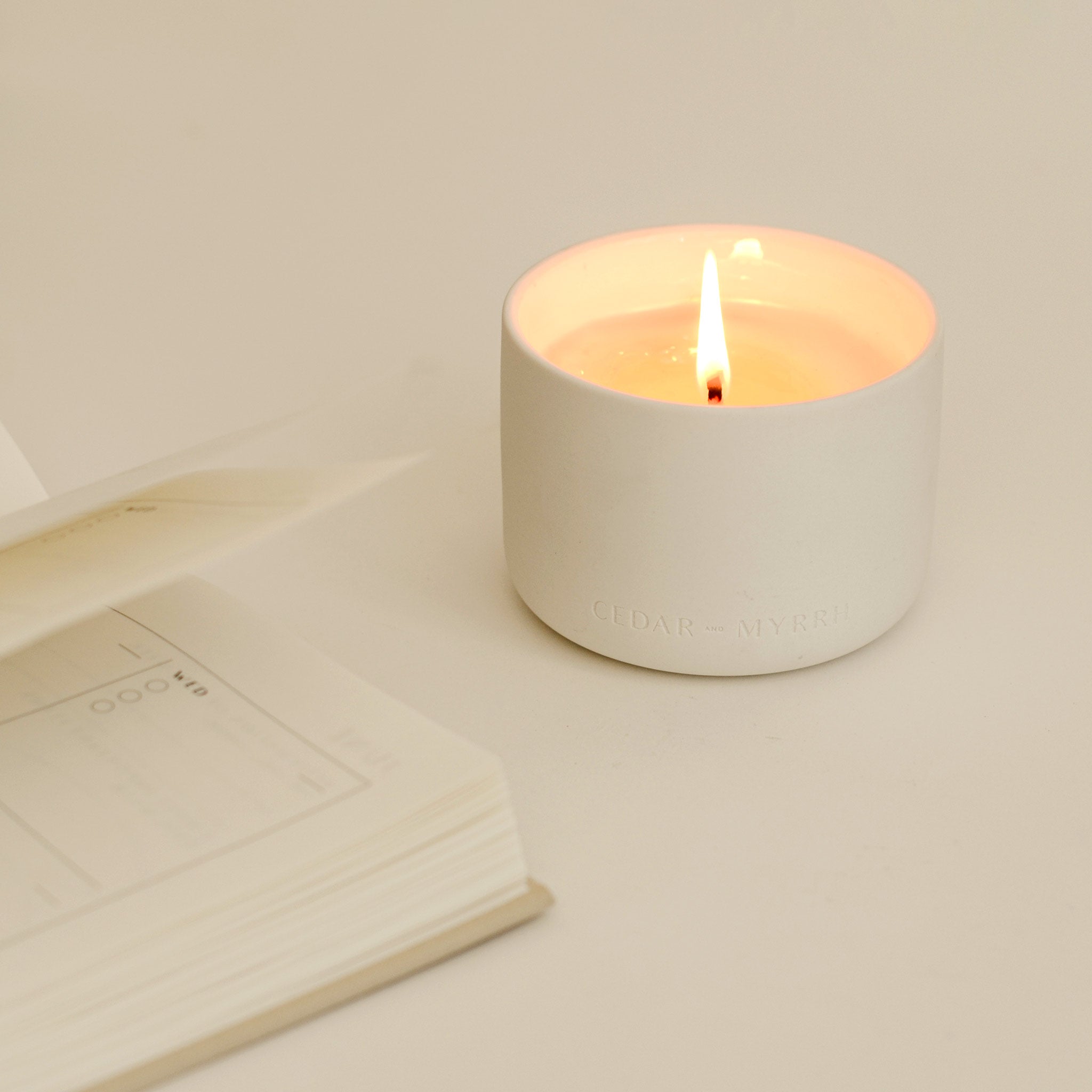 wellness candle with a lit cotton wick next to an open book.