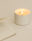 wellness candle with a lit cotton wick next to an open book.