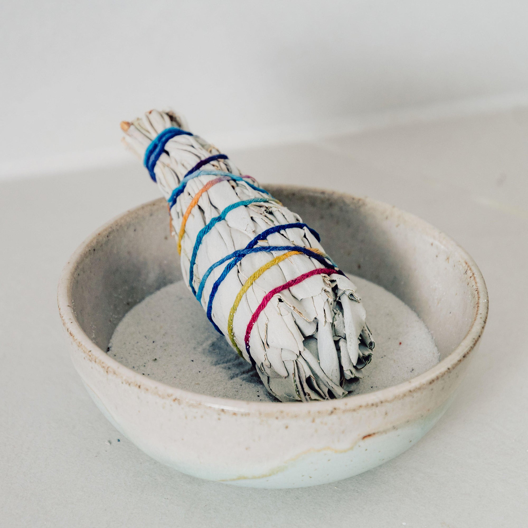 White sage smudge stick and smudging bowl with sand.